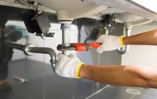 Plumber fixing white sink pipe with adjustable wrench.